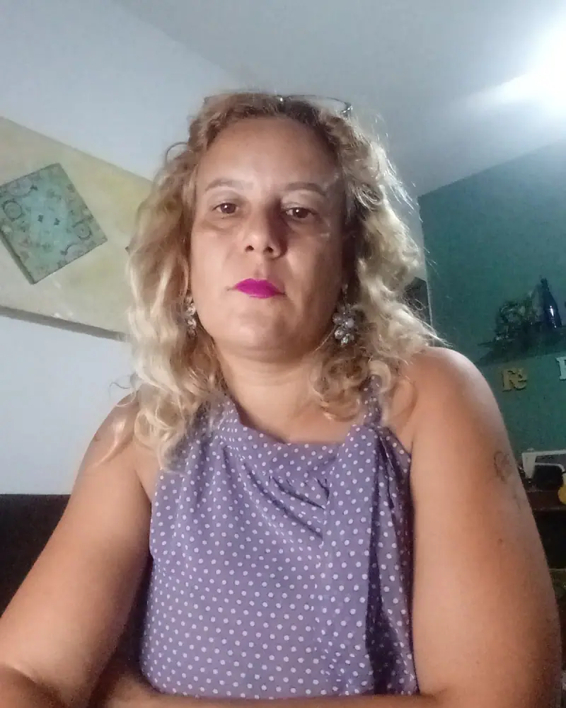 Lucila Celete, terapeuta holística, sentada, de blusa lilás, olhando para a câmera