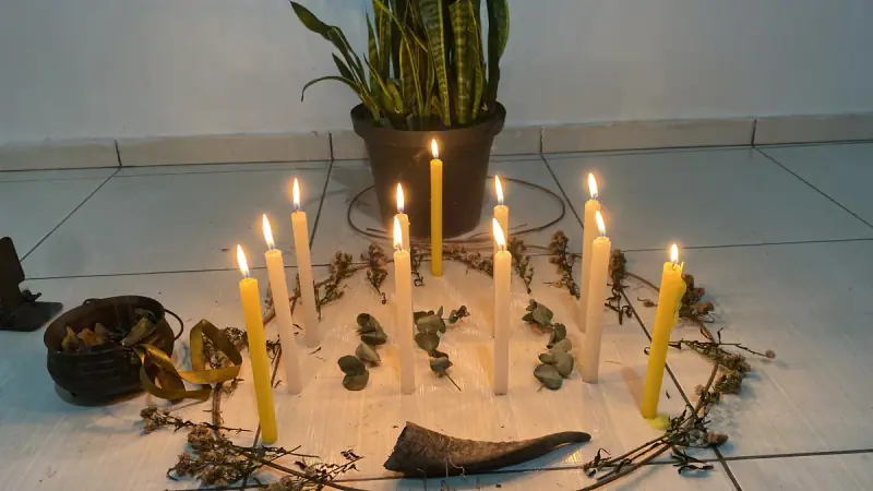 Círculo de velas amarelas acesas na areia, cercado de ramos de ervas