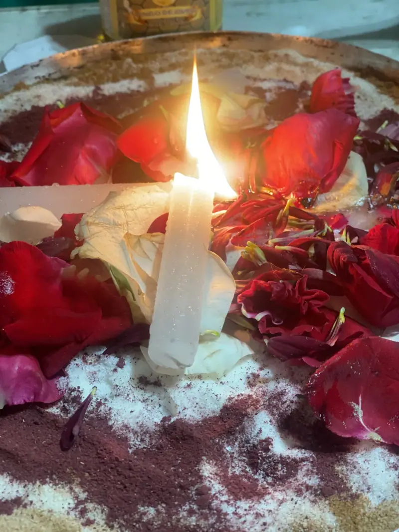 Vela branca acesa sobre pétalas de rosas vermelhas